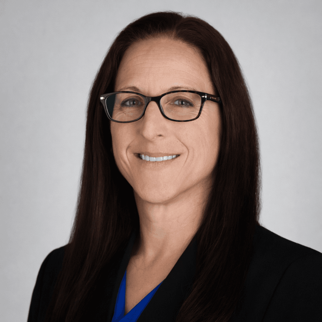 Professional headshot of a smiling woman with long dark hair, glasses, and a black blazer.